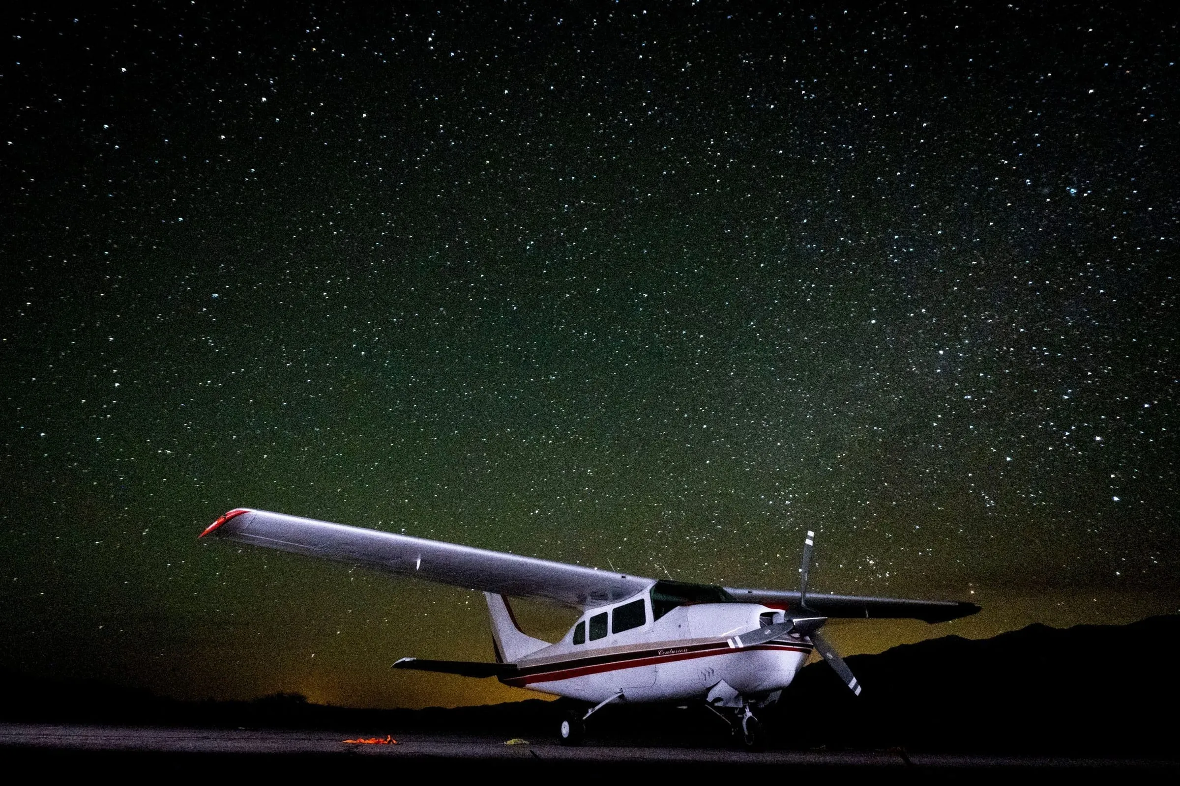 A high-wing single-engine airplane parked on a desert airstrip at night under a sky full of stars